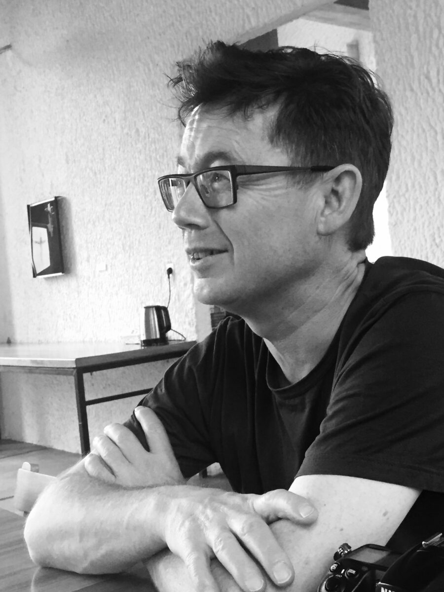 A side profile view of a smiling man wearing glasses.