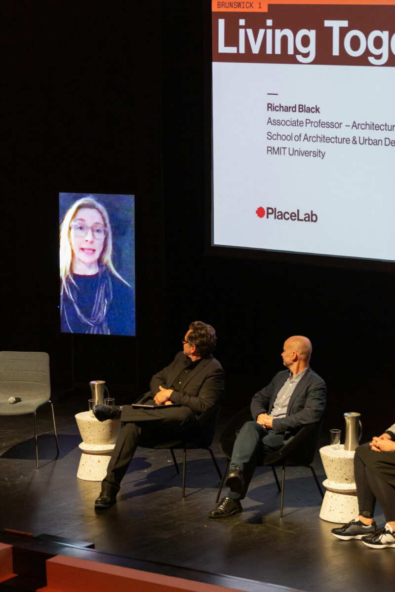 A panel discussion includes a woman on a screen giving a speech online.