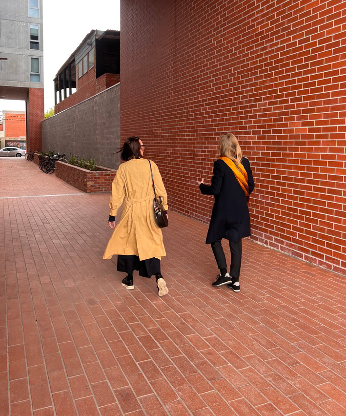 Two women walking along a red brick walkway.