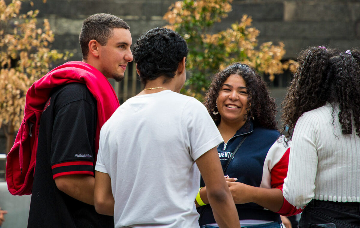 3 figures stand together talking. A person smiles at the camera.