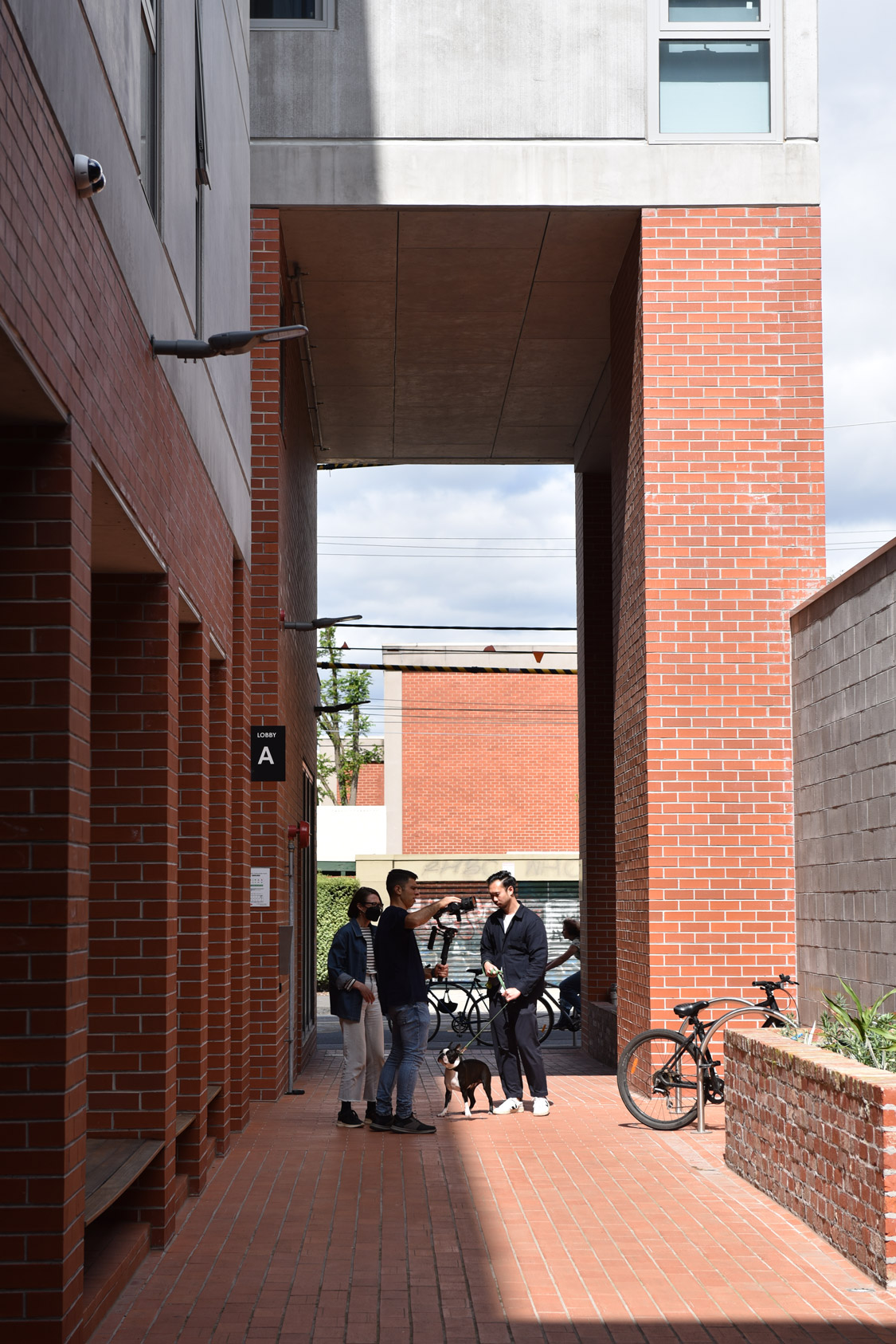 Three people filming in a red brick laneway.