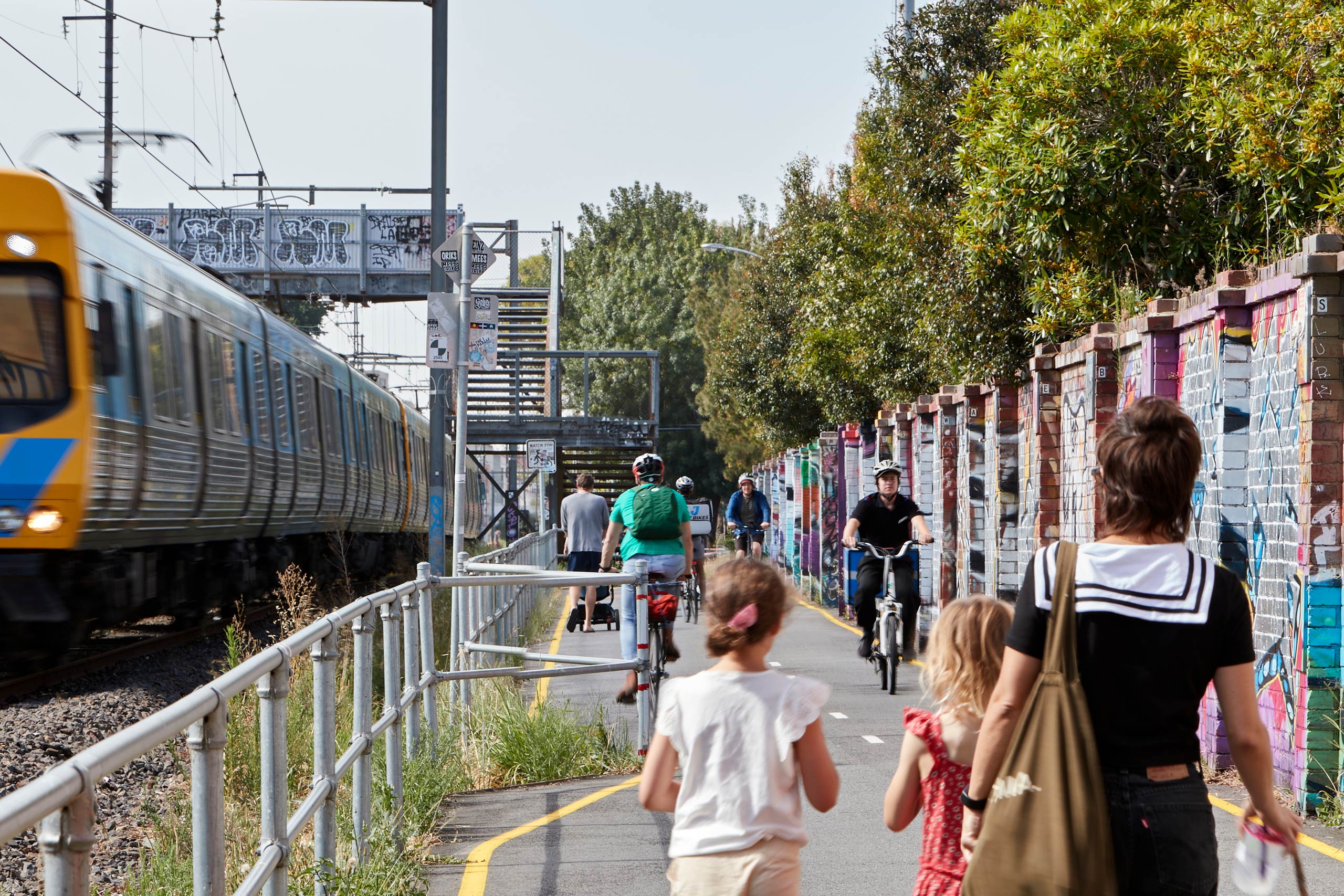 People walking and people on bikes riding on path with train moving on left hand side.